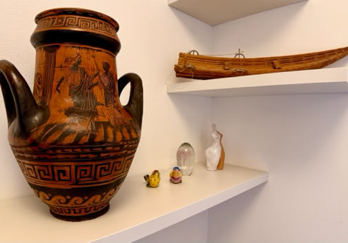 Vaso decorato su uno scaffale bianco con piccoli oggetti e una scultura di legno su un altro scaffale.