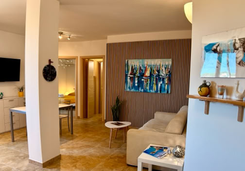 Soggiorno moderno con divano bianco, tavolino, televisore a parete, e quadri appesi.