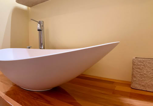 A modern white vessel sink on a wooden countertop with a silver faucet and a textured soap dispenser.