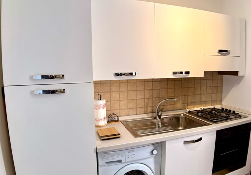 Compact kitchen with white cabinets, a stainless steel sink, a washing machine, a gas stove, and a tiled backsplash.