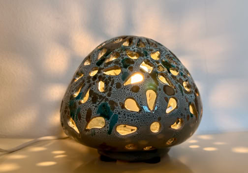 A decorative lamp with a perforated design casting intricate light patterns on a wall.